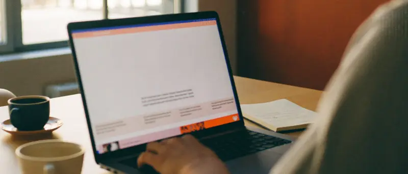A marketing lead reviewing a draft page on a laptop at a sunlit desk