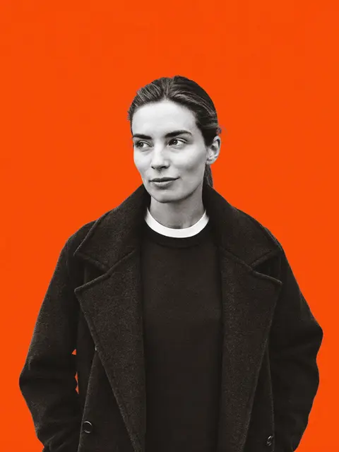 An agency strategist in a dark coat, editorial portrait on an orange backdrop